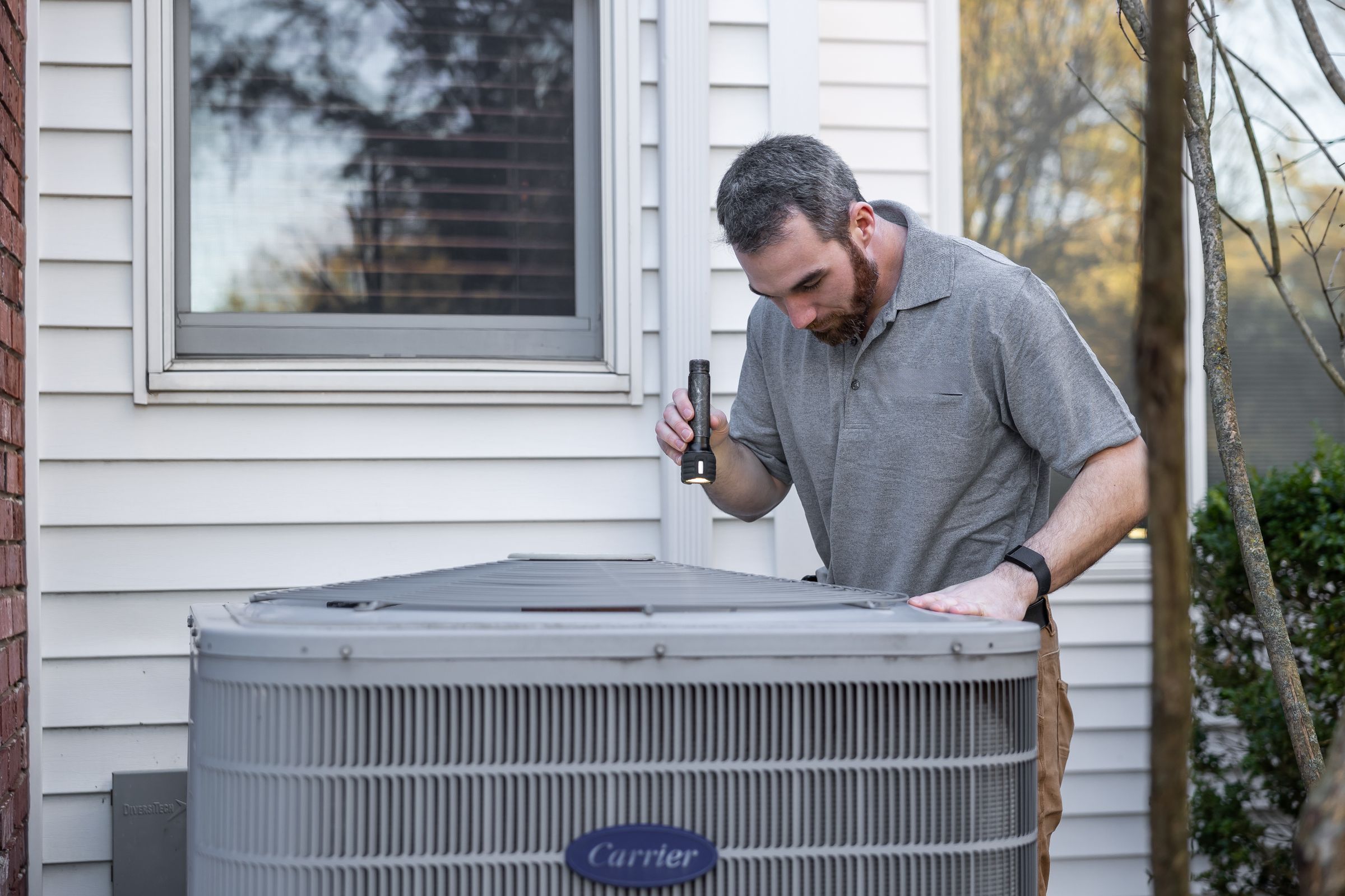 Technician inspecting an outdoor air conditioning condenser at a home